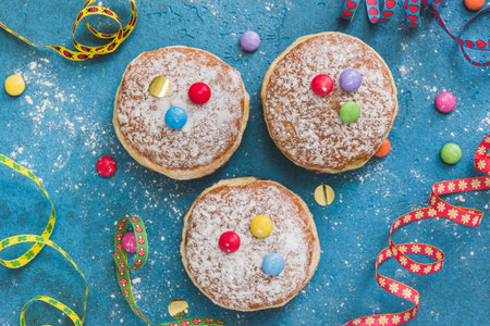 Krapfen, Berliner or donuts with streamers, confetti and chocolate beans on blue background. Colorful carnival or birthday image, top view.の写真素材