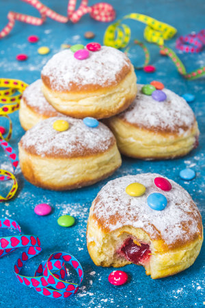 Krapfen, Berliner or donuts with streamers, confetti and chocolate beans. Colorful carnival or birthday image on blue background, vertical.の写真素材