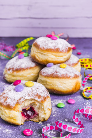 Krapfen, Berliner or donuts with streamers, confetti and chocolate beans. Colorful carnival or birthday image on purple background, vertical with copy space.の写真素材