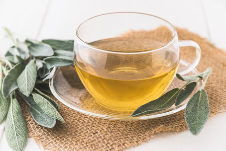 Glass cup with sage tea and sage leaves on jute and white woodの写真素材