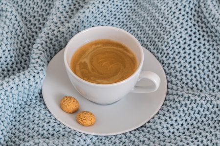 Cup of coffee on a light blue knitted wool blanket. Cozy atmosphere. Coffee break, stay at home concept.の写真素材