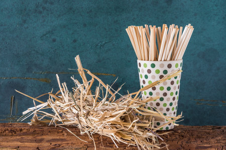 Natural straw drinking straws in a bamboo beaker and a bundle of straw on an old wooden beam, green background. Concept of sustainability, no plastic. With copy space.の写真素材