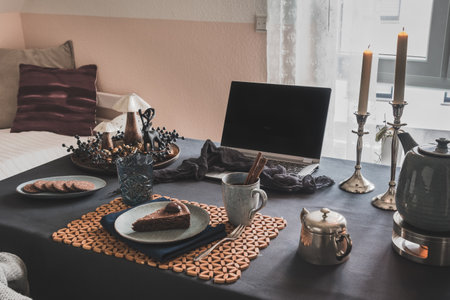 Table with laptop, cake, cookies and autumnal decoration in a cozy room prepared for virtual coffee with family or friends, useful during worldwide covid-19 pandemic quarantine timesの写真素材
