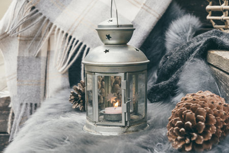 Cozy sitting area on wooden veranda with gray lambskin, lantern, fir cone and woolen scarf, gray colorsの写真素材