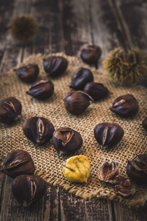 Roasted chestnuts, one peeled, on a dark wooden background, verticalの写真素材
