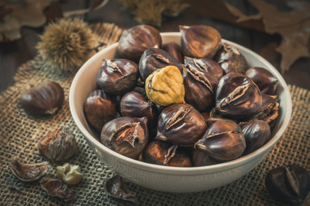 Roasted chestnuts in a bowl, one peeled, on a dark wooden backgroundの写真素材