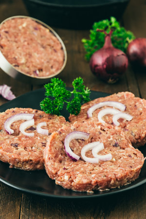 Raw homemade burger meatballs on a black plate, one in the burger press in the background, vertical stock photoの写真素材