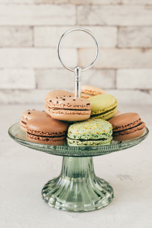 Colorful french macarons on a glass etagere in front of a white wall. Pastries, desserts and sweets. Vertical stock photo.の写真素材