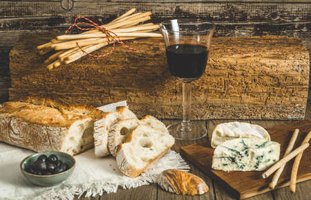 Crusty french white bread, cheese and red wine on rustic wooden table