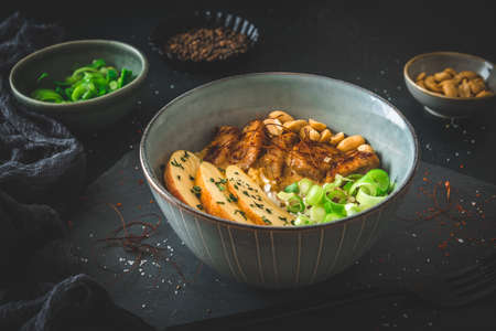 Buddha bowl with chicken, rice, peanuts, apple and chili sauce on dark backgroundの写真素材
