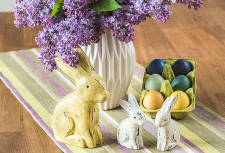 Bunch of lilac in a vase, wooden bunny family and colored eggs on an easter table. Vertical.