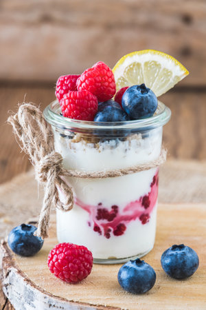 Yogurt with berries and cereals in a glass on a rustic wooden table, verticalの写真素材