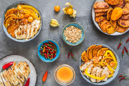 Buddha bowls with spicy chicken, rice, bell pepper, sweet potato and minced peanuts, trend and healthy food, top view on gray backgroundの写真素材