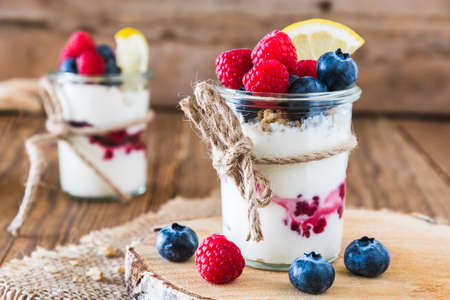 Yogurt with berries and cereals in a glass on a rustic wooden tableの写真素材