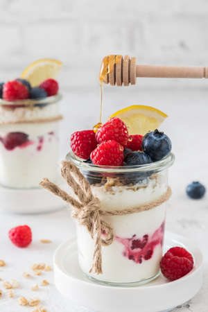 Yogurt with berries, cereals and honey in a glass on white background, verticalの写真素材
