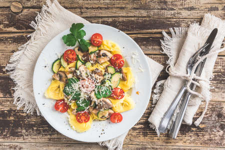 Italian cuisine: Tortellini with vegetarian mushroom cream sauce, zucchini, fresh cherry tomatoes and parmesan cheese on a rustic wooden table, top viewの写真素材