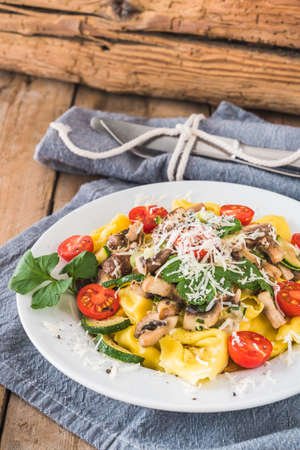 Italian cuisine: Tortellini with vegetarian mushroom cream sauce, zucchini and fresh cherry tomatoes on a rustic wooden table, verticalの写真素材