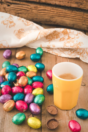 Cup of espresso and colorful wrapped easter chocolate eggs on a rustic wooden table, verticalの写真素材