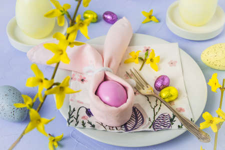 Easter table decorated with napkins and egg as an Easter bunny, egg candles and fresh forsythia...