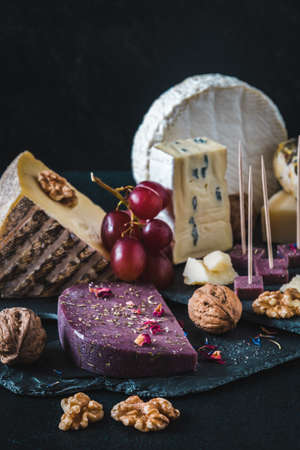 Variety of exclusive and colorful cheese, decorated with red grapes, on black background, verticalの写真素材