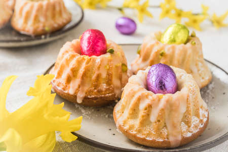 Homemade delicious mini lemon bundt cakes (muffins) with chocolate eggs on a table with spring blossoms.の写真素材