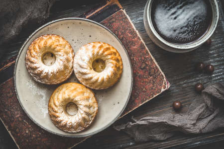 Three homemade mini bundt cakes on a plate, a cup of coffee and an old book on wooden background, top viewの写真素材