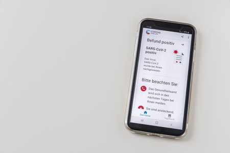 Germany - March 27th 2021: Smartphone with a positive Covid-19 SARS-CoV-2 test result in the official German Corona warning app of Robert Koch institute, white background. Result positive = result positive, Please note = Please note.のeditorial素材