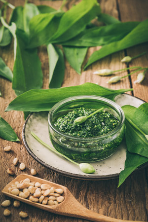 Homemade wild garlic pesto in a glass bowl on wooden background, decorated with leaves and pine nuts, desaturated colors, verticalの写真素材