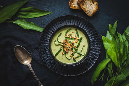 Wild garlic soup with wild garlic leaves and rosted onions on black background, top viewの写真素材
