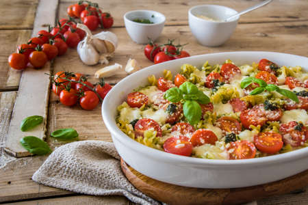 Pasta casserole with basil pesto sauce, tomatoes and mozzarella, vegetarian, on an old wooden tableの写真素材