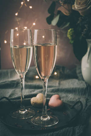 Two glasses with sparkling wine and heart shaped macarons, dimmed light, romantic atmosphere, verticalの写真素材