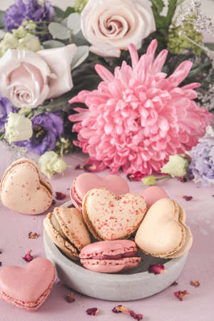 Heart shaped sweet macarons and flowers in pastel colors on a pink background. A delicious dessert or gift for Valentine's Day or Mother's Day. Vertical.の写真素材
