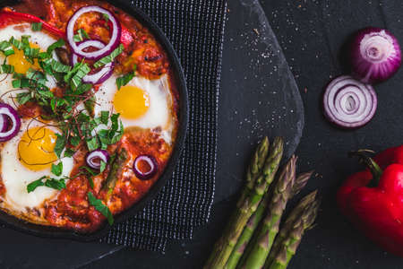 Shakshuka in an iron pan. Middle eastern traditional dish. Fried eggs with tomatoes, bell pepper, vegetables and herbs, sunny side up eggs. Top view.の写真素材