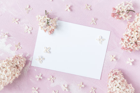 White card for text with pink lilac flowers on light pink background, top view with copy space
