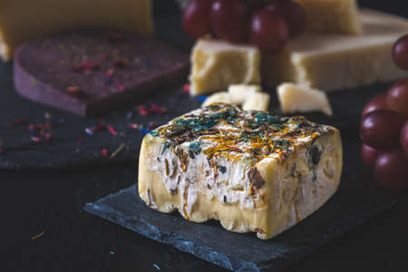 Square piece of soft cheese with colored edible flower petals on a slate plateの写真素材