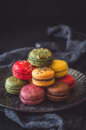 Colorful french macarons on a black plate, vertical with copy spaceの写真素材