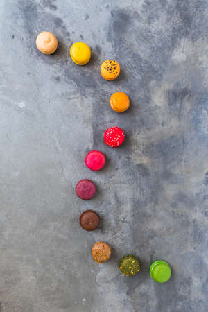 A winding row of colorful macarons on gray concrete background, top view with copy spaceの写真素材