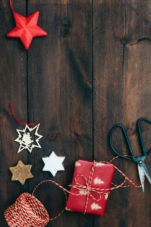 Christmas gift scene with present, ribbon, paper, cookies and decoration on rustic dark wood, top view with copy spaceの写真素材