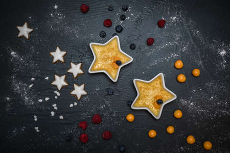 Creme brulee - traditional french vanilla cream dessert with caramelized sugar on top, served with berries and christmas cookies on black background, top viewの写真素材