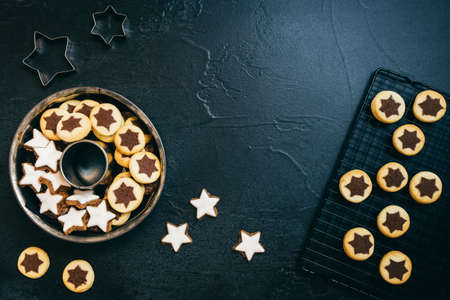 Top view on different christmas cookies, lying in a baking pan and on a cooling rost, dark gray backgroundの写真素材