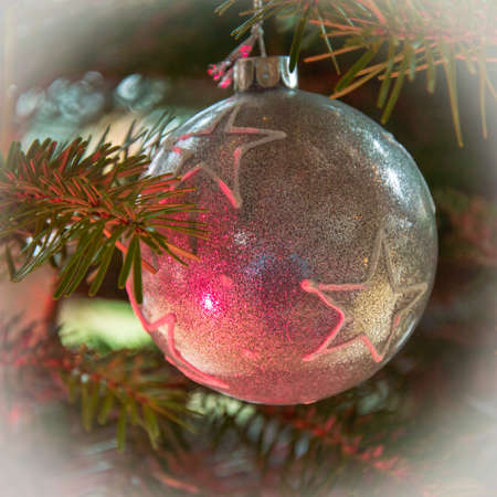 Beautiful silver textured christmas bauble with white stars at a fir tree with pink light reflectionの写真素材