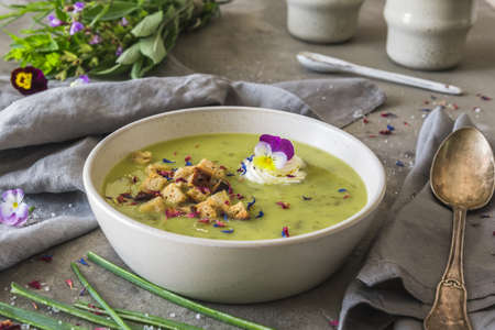 Creamy herbes soup with sorrel, edible blooms and croutons as topping. Gray concrete background.の写真素材