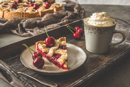 A piece of fresh cherry pie and a cup of coffee with cream on a wooden trayの写真素材
