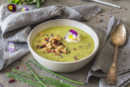 Creamy herbes soup with potatoes, herbes and sorrel, with edible blooms and croutons as topping. Gray concrete background.の写真素材