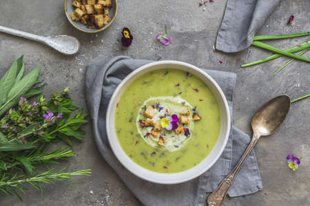 Creamy herbes soup with sorrel, edible blooms and croutons as topping. Gray concrete background. Top view.の写真素材