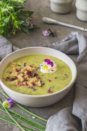 Creamy herbes soup with potatoes, herbes and sorrel, with edible blooms and croutons as topping. Gray concrete background. Vertical.の写真素材