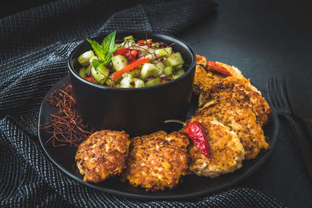Fresh cucumber salad in a black bowl with fish or vegetable patties or meatballs aroundの写真素材
