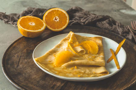 Crepe Suzette, french thin pancake with orange sauce and fruits, on a wooden plate on gray concrete backgroundの写真素材