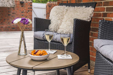 Rattan chair with cushions and a small table with wine glasses on a wooden terrace, stone wall in the backgroundの写真素材