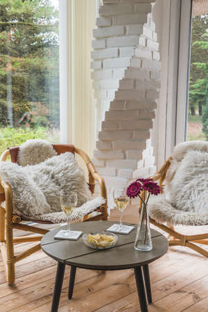 Two wicker chairs with pillows and a coffee table with wine glasses and a snack in a winter garden, verticalの写真素材